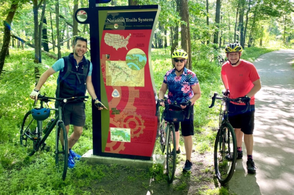 three bicycle riders with trail sign